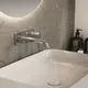 Wand-Waschtischarmatur aus Chrom von Ideal Standard, integriert in eine moderne Badumgebung mit rechteckigem Waschbecken und einem grauen Wandbelag.